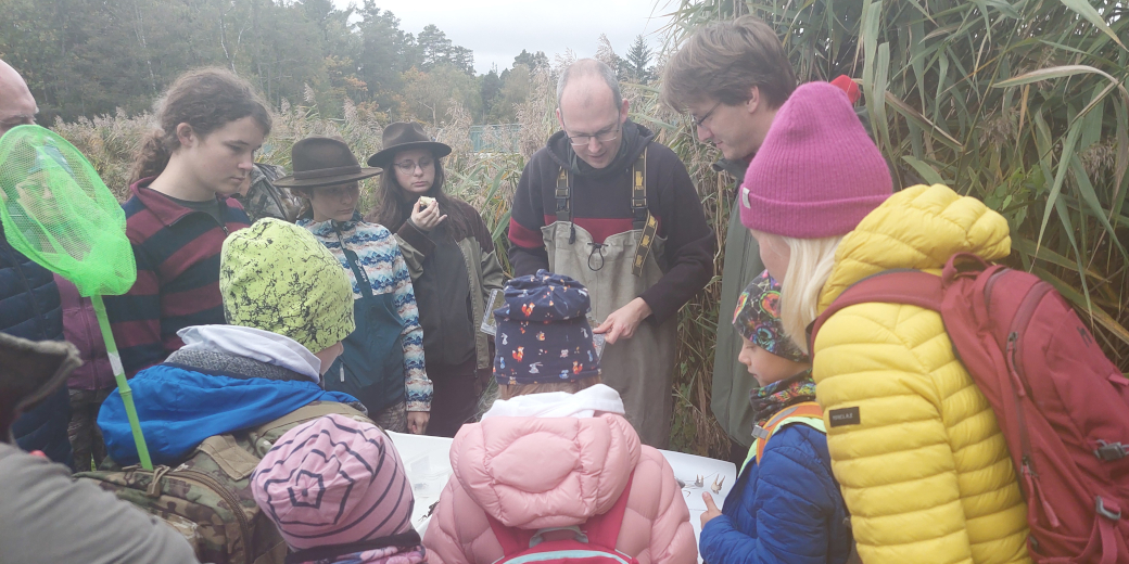 Účastníci Vycházky za raky stojí okolo stolku, u kterého probíhá povídání o racích a ukázka odchycených raků.